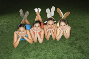 Four Smiling Young Girls laying on green lawn 